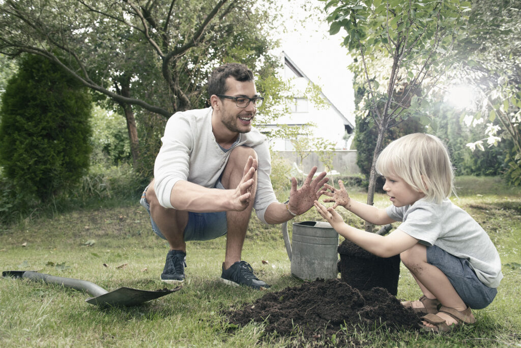 Mann und Kind pflanzen Baum ein – beim Strompreis sparen mit Solarstrom