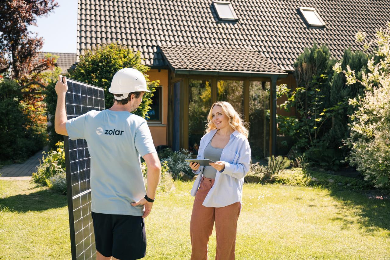 zolar-Mitarbeiter mit Solarzelle steht vor glücklicher Kundin